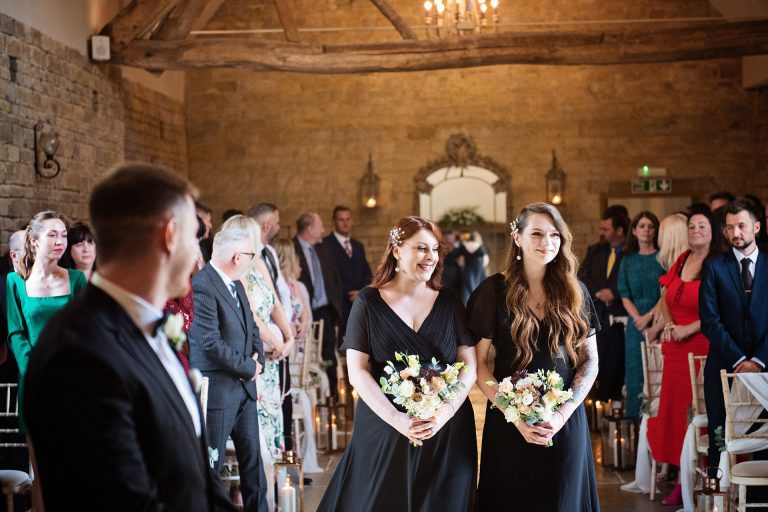 Bridesmaids walking down the wedding isle smiling at Blackwell Grange.