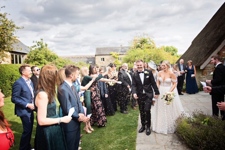 Candid photo by Blooming Photography taken at Blackwell Grange. Bride and groom getting showered by their guests in confetti.