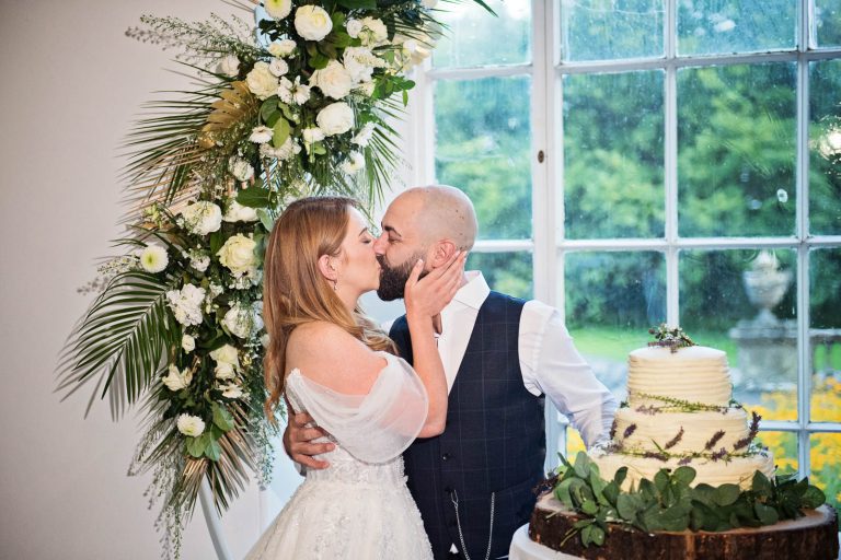 Candid photo of bride and groom kissing after cutting their wedding cake at Margam Country Park, taken by Blooming Photography.