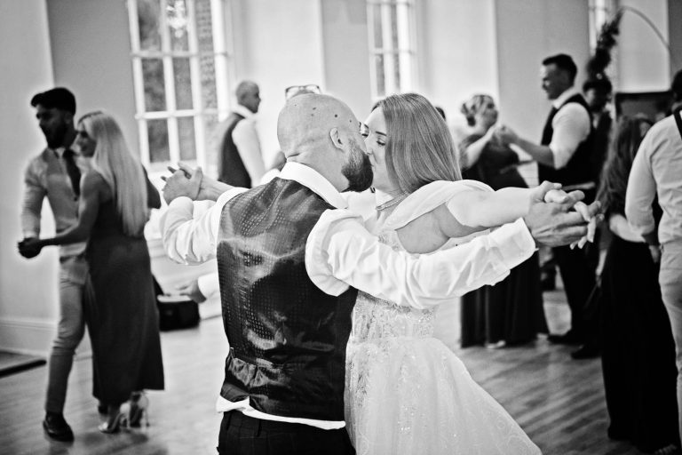 Candid B&W photo of bride and groom dancing and kissing at Margam Country Park, taken by Blooming Photography.