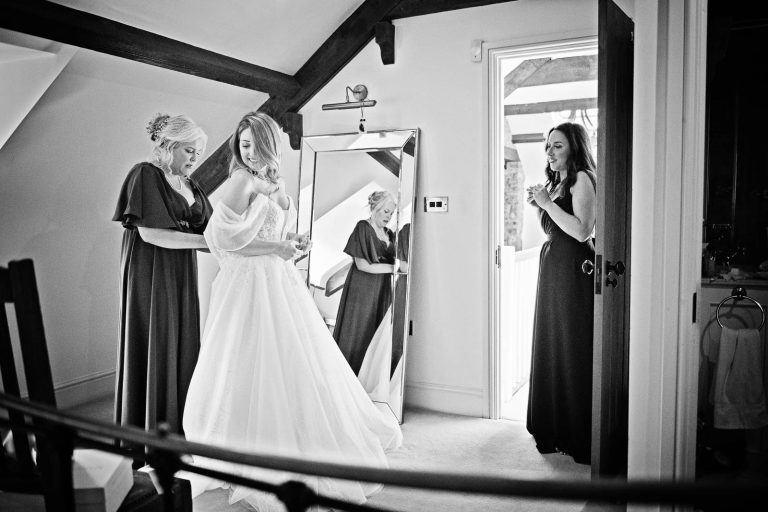 Black and white documentary photo of bride putting on her wedding dress by Cardiff wedding photographer, Blooming Photography