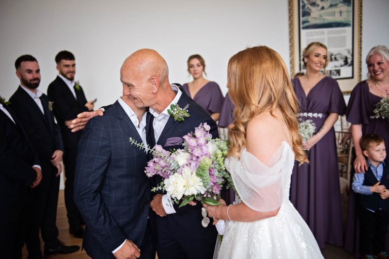 Candid photo of a father of the bride hugging the groom at a wedding ceremony at Margam Country Park. Photographed by Blooming Photography