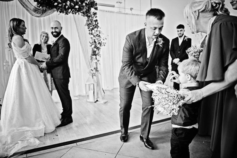 Candid Black & white photo of a ring boy exchanging the rings at a wedding at Margam Country Park. Photographed by Blooming Photography