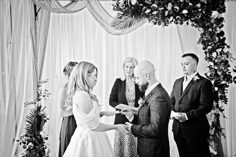 Candid Black & white photo of a bride and groom exchanging rings at a wedding at Margam Country Park. Photographed by Blooming Photography