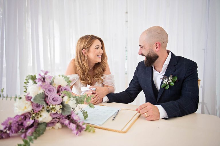 Bride and groom smiling at each other after signing the wedding register. Photographed by Blooming Photography at a wedding at Margam Country Park.
