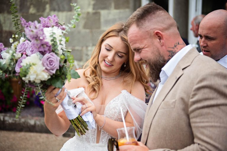 Candid photo taken of a bride talking to her brother and showing the details of a wedding bouquet at a wedding at Margam Country Park by Blooming Photography.