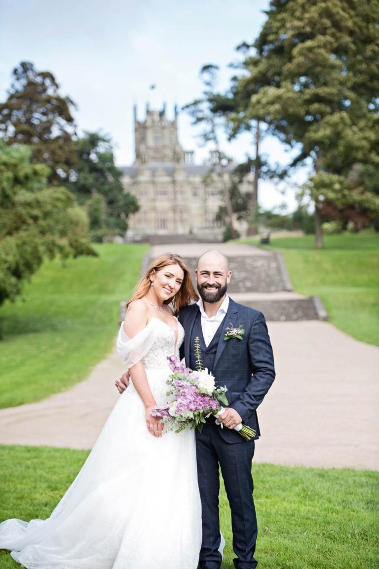 Wedding photo of bride and groom holding each other closely, smiling with Margam Country Park behind them - photo by Blooming Photography.