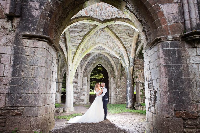 Amazing photo of bride and groom kissing under arches that are lit up. Photo taken at Margam Country Park by Blooming Photography.