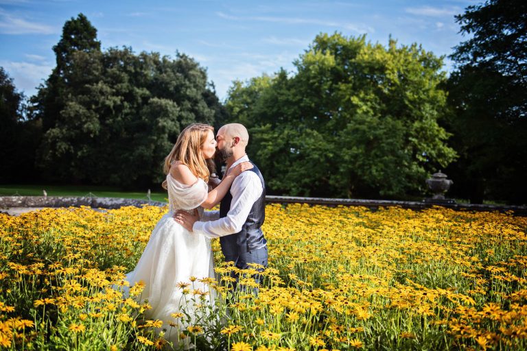Candid wedding photograph of bride and groom kissing in a bank of yellow daisy flowers at Margam Country Park photo by Blooming Photography.