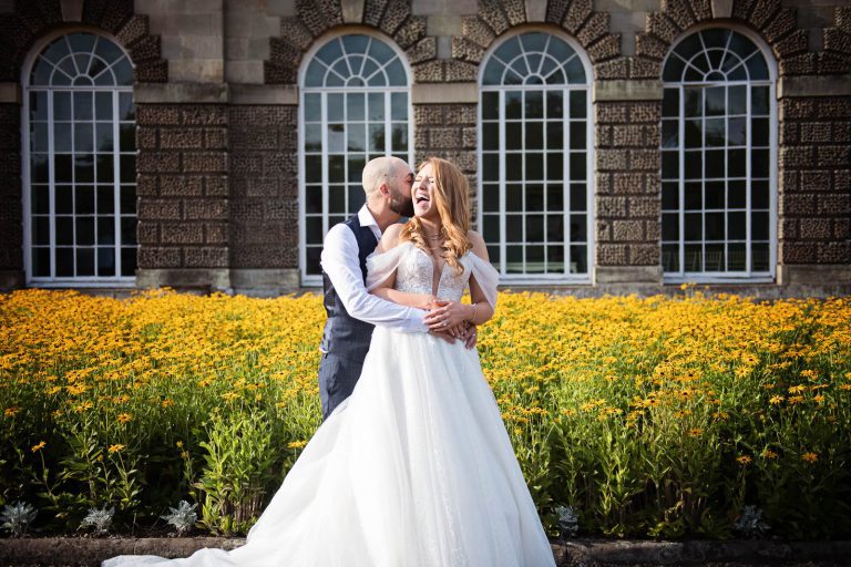 Candid wedding photograph of bride and groom hugging a laughing at Margam Country Park photo by Blooming Photography.