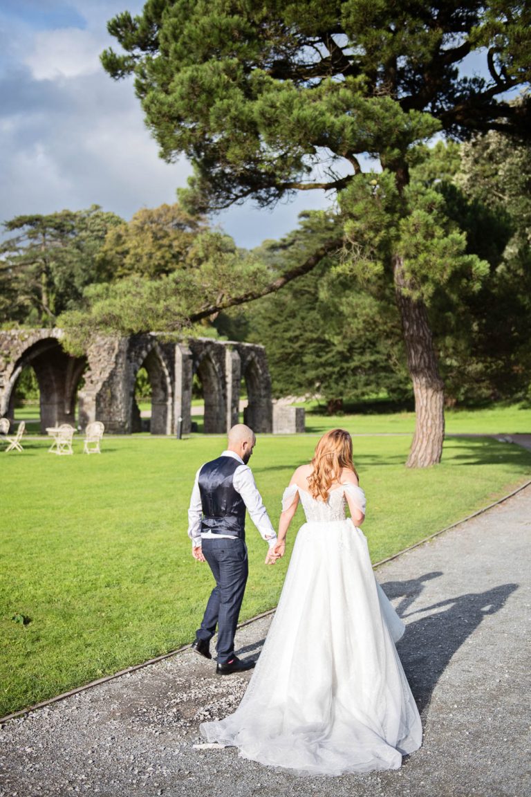 Candid wedding photography of bride and groom holding hands and walking away down a path at Margam Country Park photo by Blooming Photography.