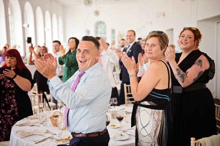 Candid image taken of friends cheering as the bride and groom enter the wedding breakfast at Margam Country Park, by Blooming Photography.