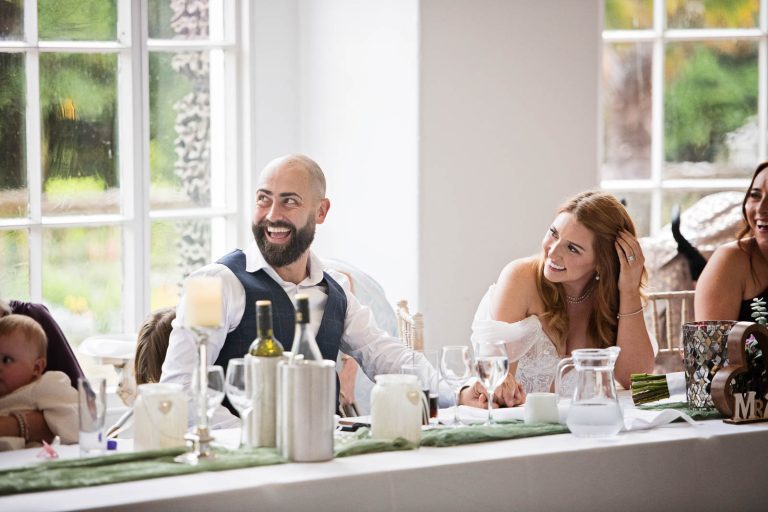 Candid image taken of groom and bride laughing at Margam Country Park, during the wedding speeches by Blooming Photography.