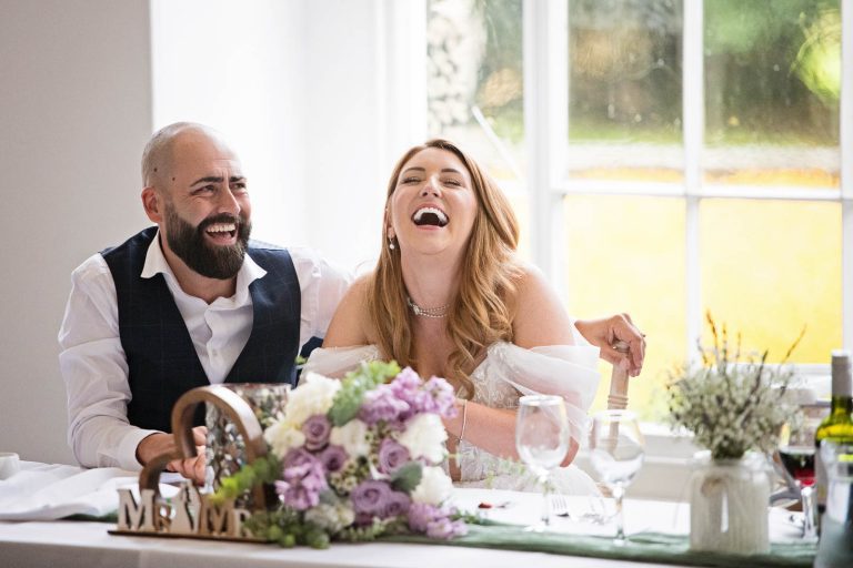 Candid image of bride and groom laughing taken at Margam Country Park, during the wedding speeches by Blooming Photography.