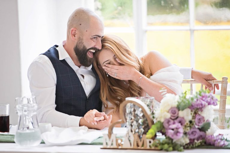 Candid image of the bride and groom laughing together taken at Margam Country Park, during the wedding speeches by Blooming Photography.