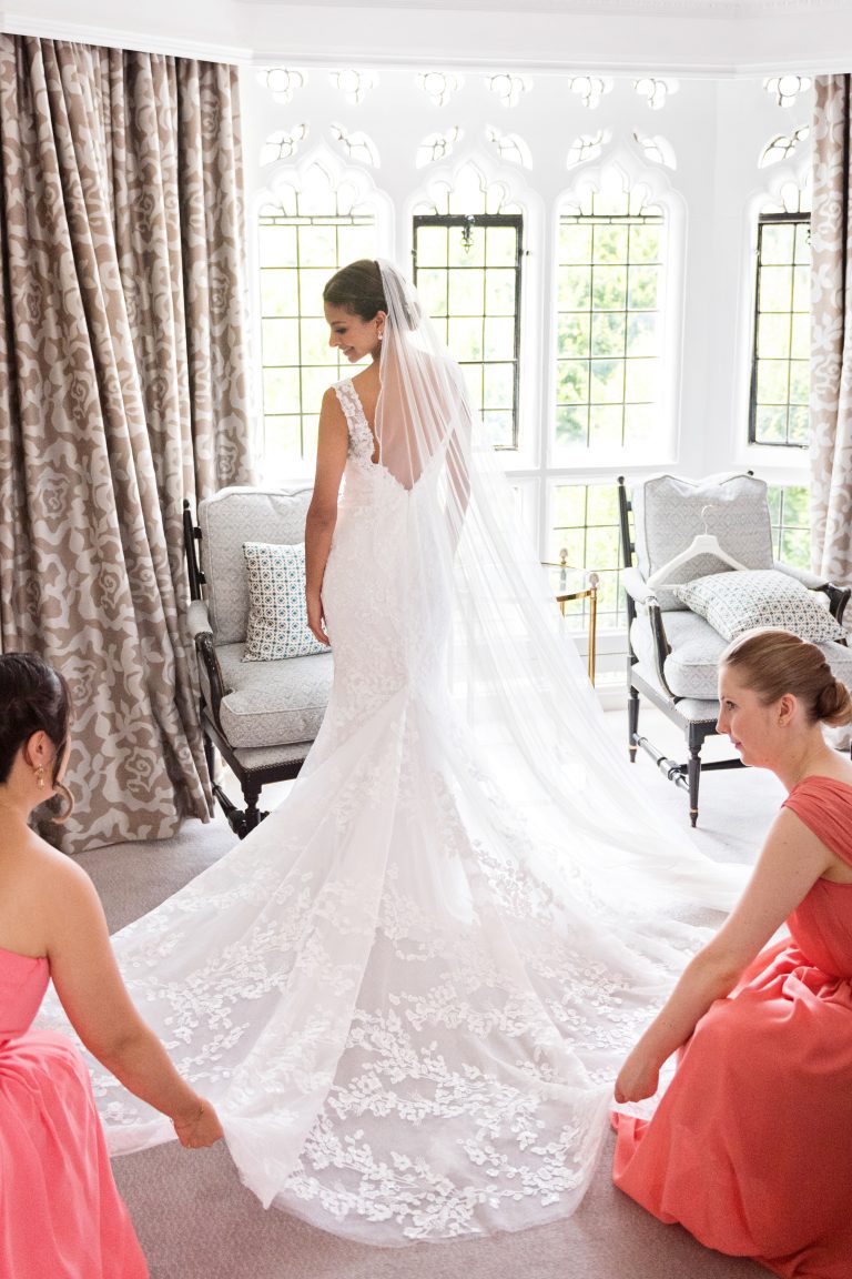 Bridesmaids lay the brides wedding dress out. Bride looking over her shoulder. Gorgeous. Photography by Blooming Photography at Danesfield House Hotel and Spa.