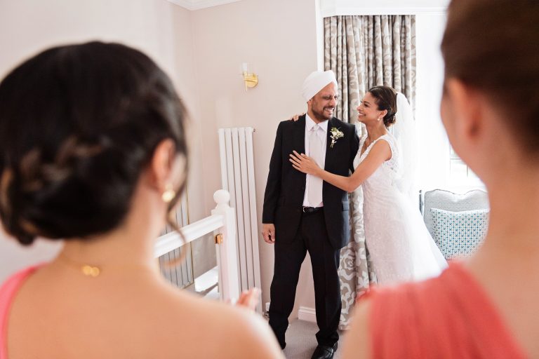 The bride hugs her father in the first look. Bridesmaids look onward and give the photo good composition. Photography by Blooming Photography at Danesfield House Hotel and Spa.