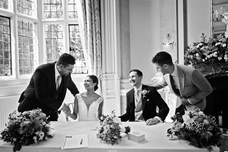 Bride and groom get congratulated by their witness'. Black and white photograph. Photography by Blooming Photography at Danesfield House Hotel and Spa.