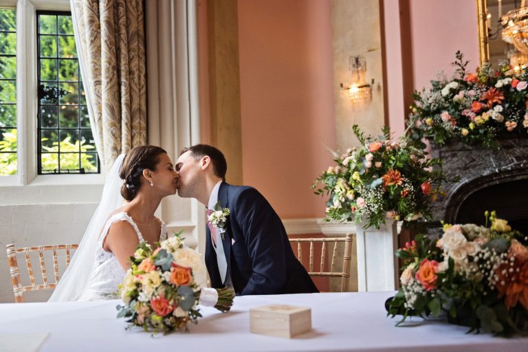 A bride and groom kiss after signing the marriage certificate. Photography by Blooming Photography at Danesfield House Hotel and Spa.