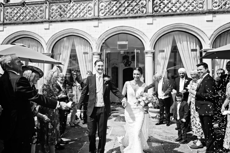 A timeless black and white photograph of the bride and groom walking down a confetti isle made by family and friends at Danesfield House Hotel and Spa. Photography by Blooming Photography.