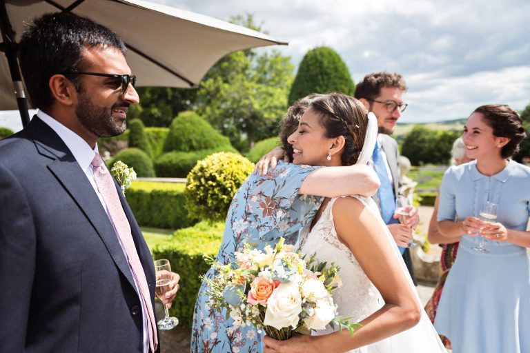 Candid photograph of the bride being hugged by a family member in the gardens of Danesfield House Hotel and Spa. Photography by Ben Roberts Blooming Photography.