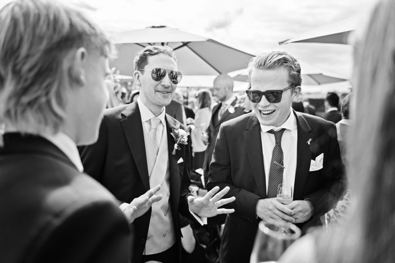 The groom and his groomsmen exchange stories and are laughing and smiling. Classic black and white image. Photographed at Danesfield House Hotel and Spa. Photography by Ben Roberts Blooming Photography.