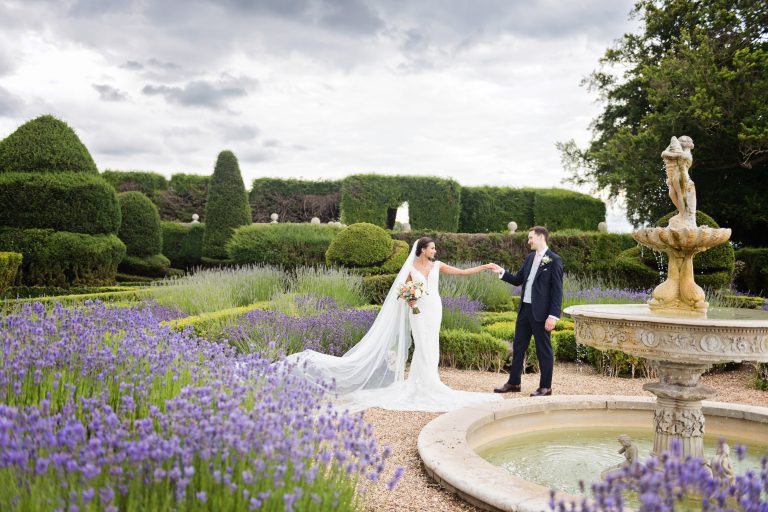 Bride and groom in the grounds at Danesfield House Hotel and Spa. Bride and groom hold hands behind the water fountain. Really elegant photograph. Photography by Ben Roberts Blooming Photography.