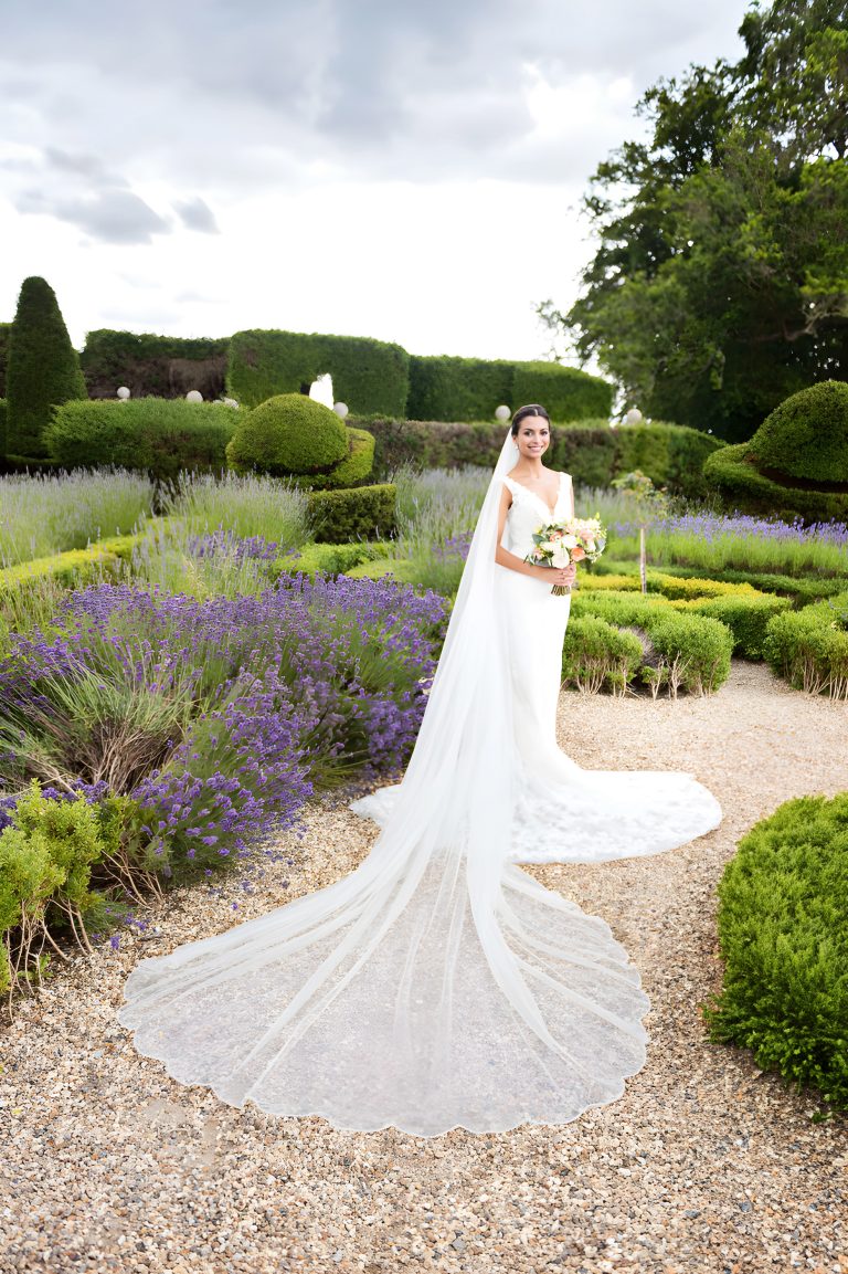 Portrait photograph of an elegant bride with her wedding veil and dress laid out. Lavender and formal gardens of Danesfield House Hotel and Spa in the background. Photography by Ben Roberts, Blooming Photography.