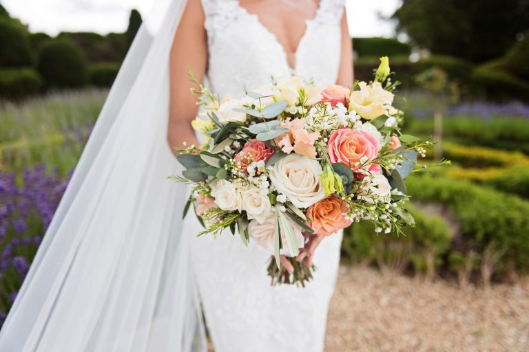 Mid centre photo of the bride, her wedding veil and wedding bouquet. The wedding bouquet is an elegant summer mix of roses, gypsophila and eucalyptus leaf. Photographed in the formal gardens of Danesfield House Hotel and Spa in the background. Photograph by Ben Roberts, Blooming Photography.