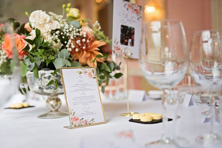Wedding breakfast details at Danesfield House Hotel and Spa ballroom. A menu, centre table flowers, wine glasses and butter adjourn the table. Photograph by Ben Roberts, Blooming Photography.