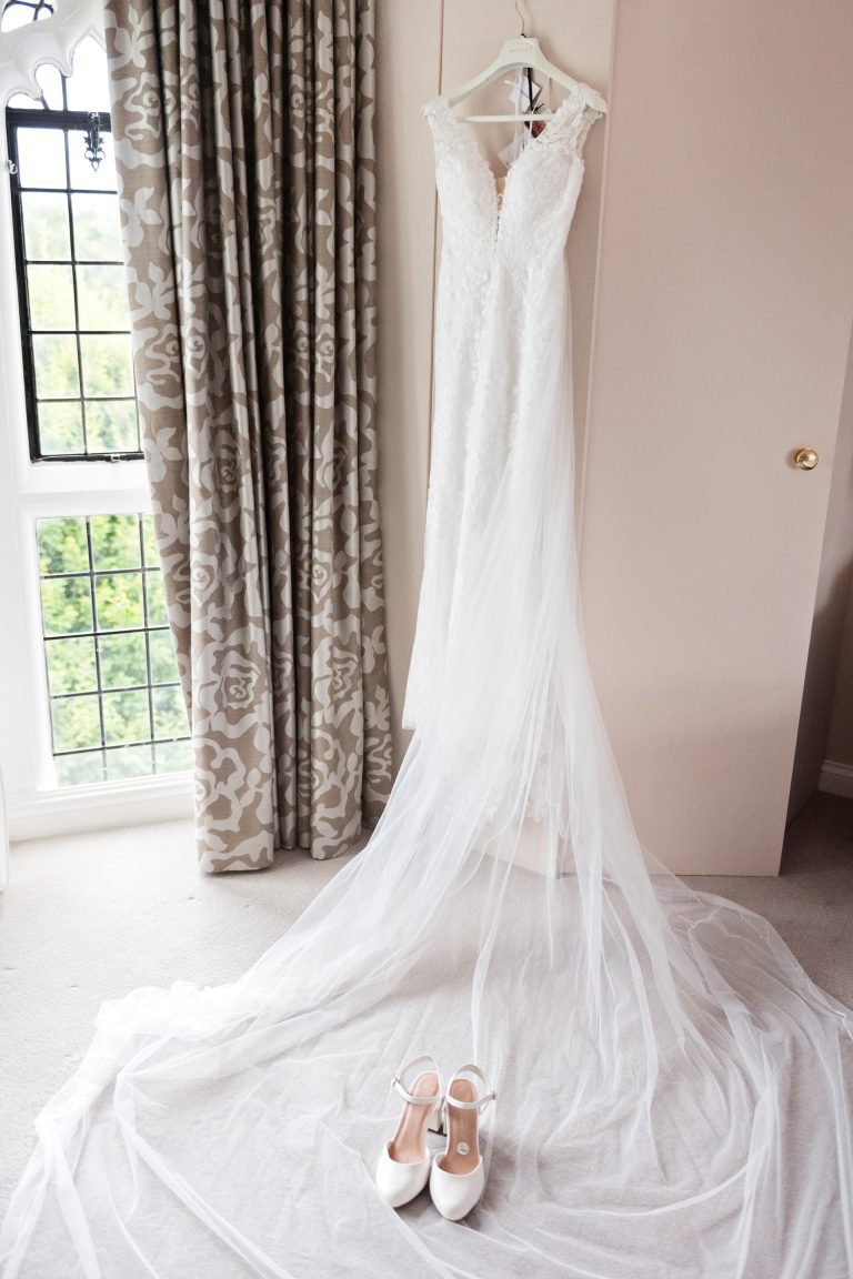 Wedding dress hung up with some wedding shoes laid on top of the train of the dress. Danesfield House Hotel and Spa. Photography by Blooming Photography.
