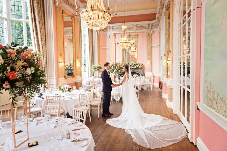 Bride and groom hold hands in the ballroom at Danesfield House Hotel and Spa. Wedding breakfast set up. Elegant. Photograph by Ben Roberts, Blooming Photography.