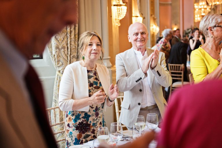 Guests clapping in a candid photo taken as the bride and groom (not seen in picture) enter Danesfield House Ballroom. Photograph by Ben Roberts, Blooming Photography.