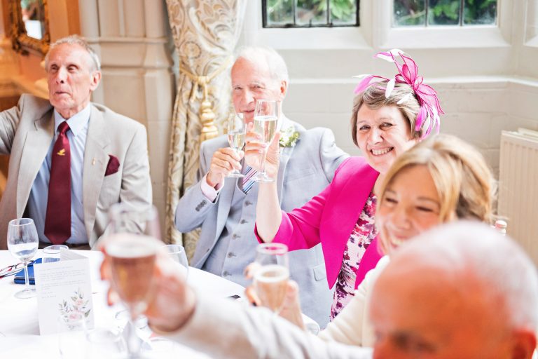 Guests including mother of the groom cheer to the grooms wedding speech. Photographed in Danesfield House Ballroom. Photograph by Ben Roberts, Blooming Photography.