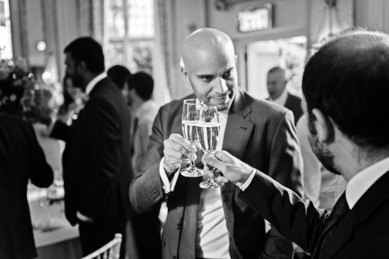 Guests "clink" their champagne glasses at the end of speeches. Black and white photo. Shot in the Danesfield House Ballroom. Photograph by Ben Roberts, Blooming Photography.