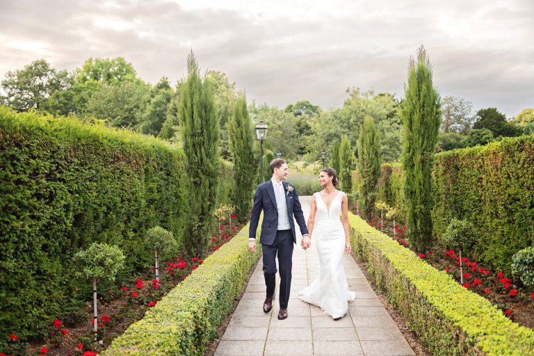Bride and groom hand-in-hand walking down a paved path at Danesfield House Hotel & Spa wedding. Photography by Blooming Photography.