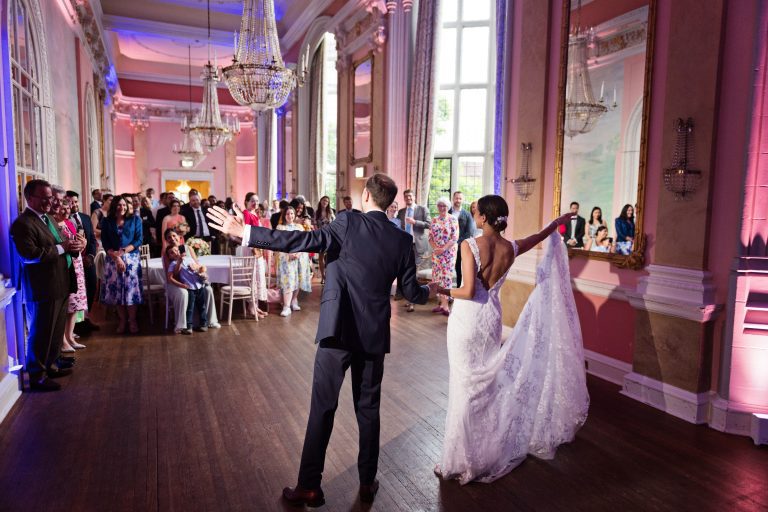 Bride and groom do their first choreographed dance. Backs facing, crowds reaction. Photographed in the elegant Danesfield House Hotel and Spa Ballroom. Photograph by Ben Roberts, Blooming Photography.
