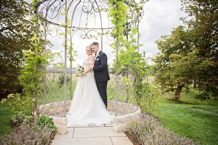 Elegant photo taken by Blooming Photography taken at Blackwell Grange of a Bride and groom hugging whilst they are in a wedding arch.