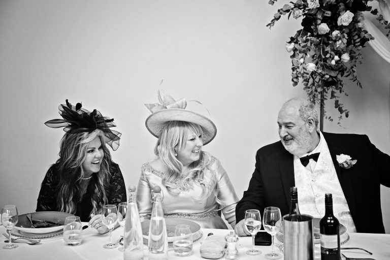 B&W image of the mother of the bride and father of the bride and auntie chatting and smiling. Candid photo by Blooming Photography. Taken at Blackwell Grange, Warwickshire.