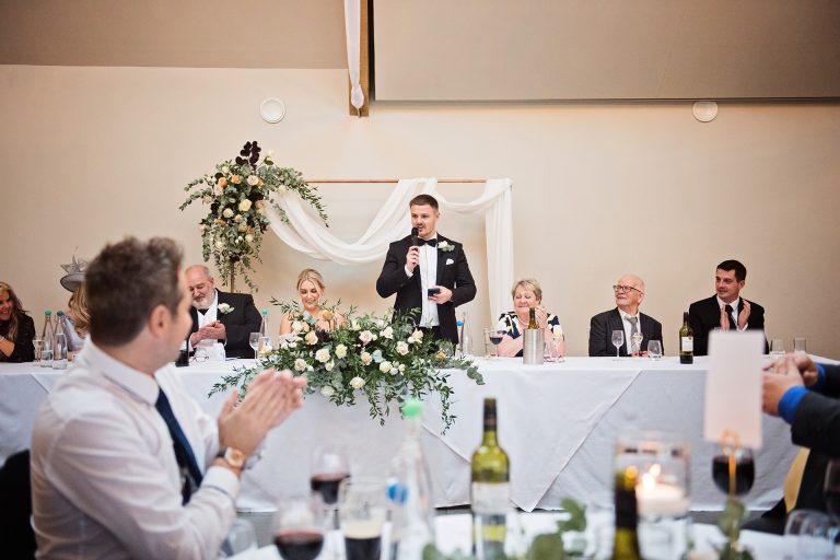 Candid photo by Blooming Photography. Taken at Blackwell Grange, Warwickshire. Groom delivering his wedding speech with guest clapping around him.