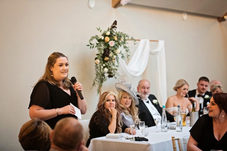 Maid of honour doing her speech. Top table including the bride is behind her. Candid photo by Blooming Photography. Taken at Blackwell Grange, Warwickshire.