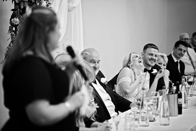 B&w image of the bride and her groom laughing at the maid of honour speech. Candid photo by Blooming Photography. Taken at Blackwell Grange, Warwickshire.