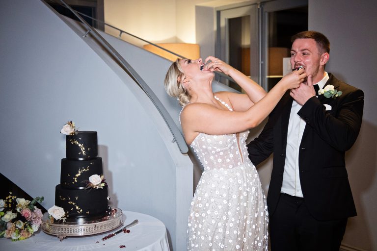 Bride and groom feed each other wedding cake. Candid photo by Blooming Photography. Taken at Blackwell Grange, Warwickshire.
