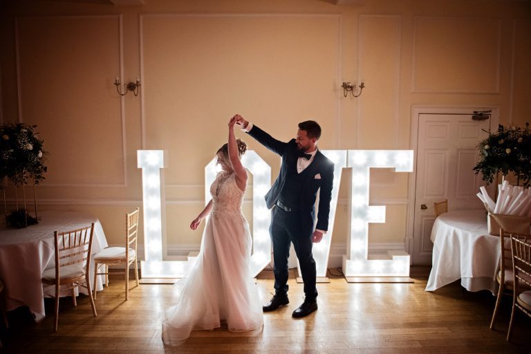 Bride and groom dance in front of a lit up Love sign at Eastington Park at a Christmas Wedding.