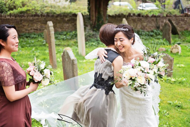 Candid photo of bride being hugged by a wedding guest. Photograph by Blooming Photography.