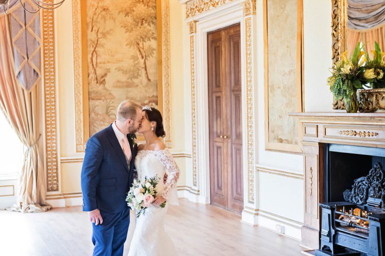 Landscape photo of Bride and groom kissing in the tapestry room in Leigh Court. Candid photograph by Blooming Photography.