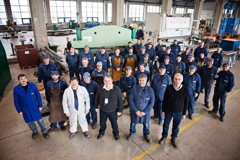 Team photograph of 30+ engineering colleagues all looking up (shot from above), smiling at the camera.
