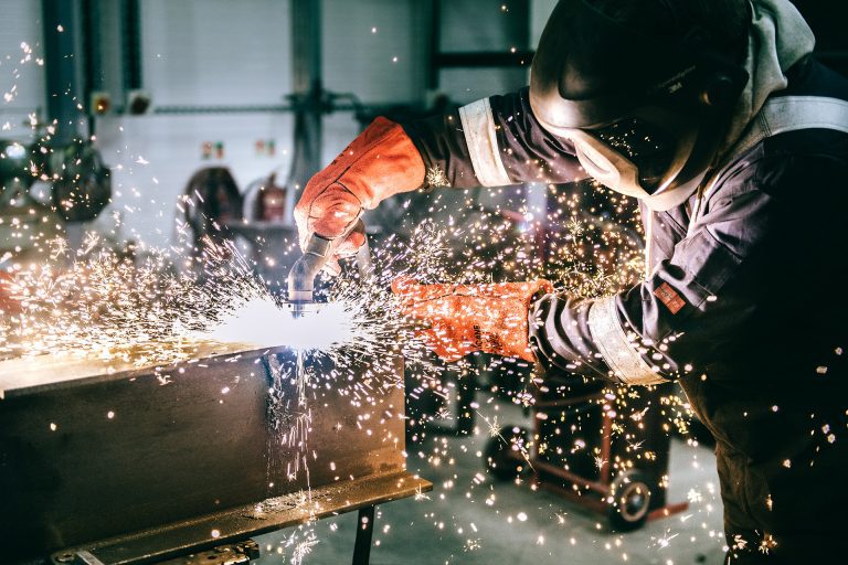 Striking image of a welder, welding a piece of steel, sparks flying. Photograph by Blooming Photography.