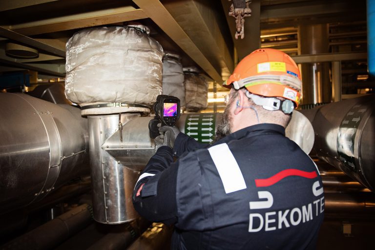 An engineer holding a heat gun to check the temperature of expansion joints in a factory setting,.