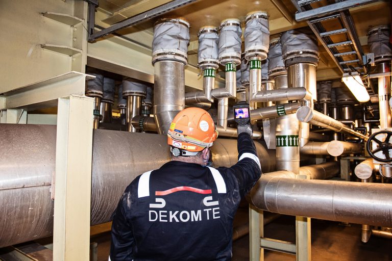 An engineer holding a heat gun to check the temperature of expansion joints in a factory setting,.